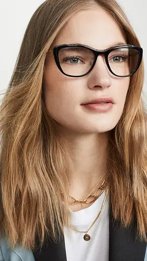 Woman wearing black glasses, a white shirt, a gold necklace, and a black blazer.