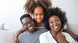A family with a man, a woman, and a young girl sitting on a couch and smiling for a photo.