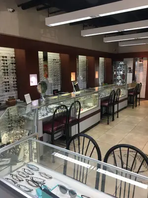 A shop interior with glass displays of glasses and other accessories, chairs, and lighting fixtures.