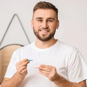 A man in a white t-shirt is holding a toothbrush and smiling for a picture.