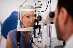 A woman is looking into a machine that is probably an eye examination machine, while a man is looking at her eye.