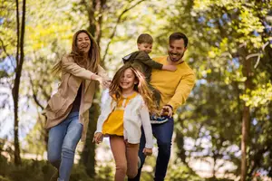 A family is walking and playing in the forest with a young boy riding on his father's back