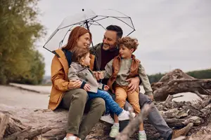 Family of four sitting on a log in the rain with an umbrella