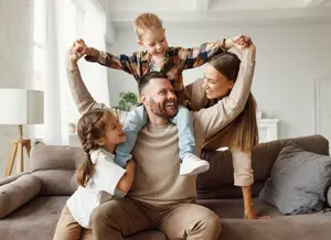 A family is sitting on a couch with a lamp and a plant in the background.