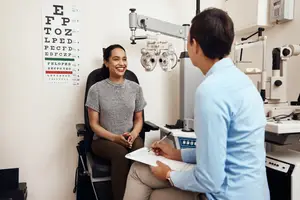 An optometrist is discussing eye care with a patient in an examination room.