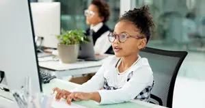 Girl sitting at a desk with a computer in front of her in an office.