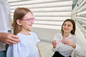 A young girl tries on glasses in an optometrist's office.
