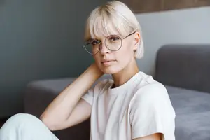 Woman sitting on a couch wearing glasses and a white t-shirt.
