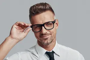A man adjusting his glasses and smiling in a studio setting.