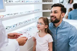 A man and a girl are in an optics store and the man is holding a pair of glasses