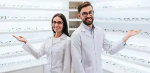 Two people in lab coats standing in front of a wall of glasses