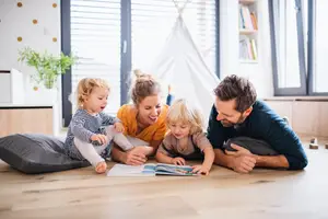 A family is sitting on the floor and reading a book together