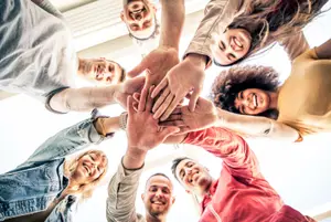 A group of people with their hands together smiling and looking up at the camera