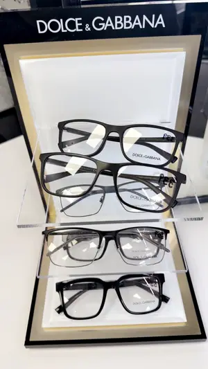 Three pairs of Dolce & Gabbana eyeglasses displayed in a black and gold frame with a clear glass shelf