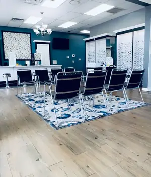 A large room with a blue wall, a chandelier, a rug, and several chairs and tables in it.