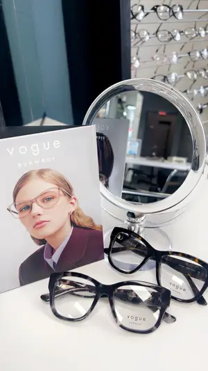 Vogue eyewear with a magazine featuring a woman with glasses on a table next to a mirror
