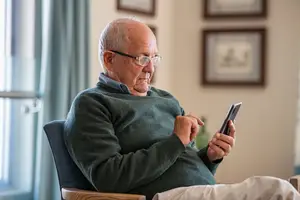 Elderly man sitting on a chair using a cell phone