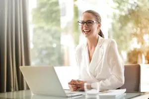 A woman sitting at a desk with a laptop and smiling for the camera.