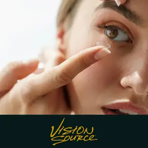Close-up of a woman inserting a contact lens into her eye with the text 'Vision Source' displayed below