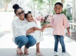 A mother and her two kids, a boy and a girl, are posing for a photo, holding flowers and smiling