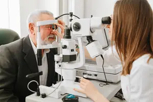 An elderly man having his eyes examined by a young female doctor in a clinic.