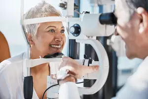 An elderly woman is undergoing an eye examination by a male doctor in a clinical setting.