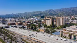 Aerial view of a city with a highway, buildings, mountains, and vehicles