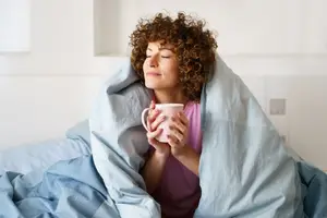 A woman with curly hair lying on a bed and holding a cup of coffee