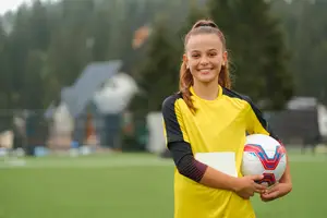 A girl holding a soccer ball in her hands on a soccer field