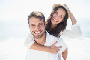 A man and a woman standing on the beach, smiling, and posing for a photo