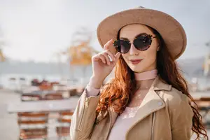 Woman in a brown jacket and hat posing for a photo by a lake