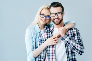 A man and woman wearing glasses are smiling and posing for a photo