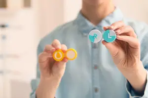 Person holding eye drops and contact lenses in their hands