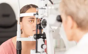 A young woman having her eyes examined by an optometrist in a clinical setting.