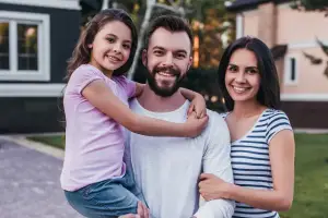 A family of three standing in front of a house, all smiling for the camera.