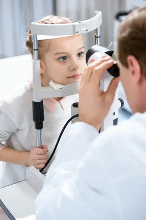 An optometrist examining a young girl's eyes using an ophthalmoscope