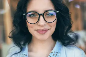 A woman wearing glasses and a denim jacket is smiling for a photo.
