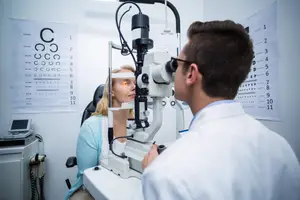A man in a white lab coat is examining a woman's eyes with a microscope in an eye clinic.