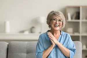 Happy senior woman sitting on the sofa in the living room with a smile on her face and looking away.