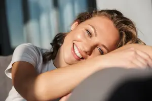 A young woman lying down on a couch smiling with her eyes closed