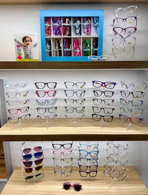 A store display of various colored eyeglasses on wooden shelves, including a book with a child wearing glasses and a blue box with multiple compartments filled with different colored glasses.