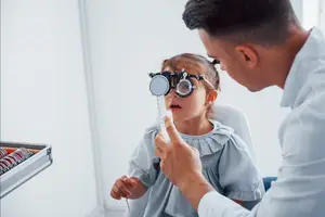 A male doctor examining a young girl's eyes using an ophthalmoscope