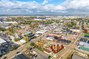 Aerial view of a town with various buildings, parking lots, and trees, under a cloudy sky.