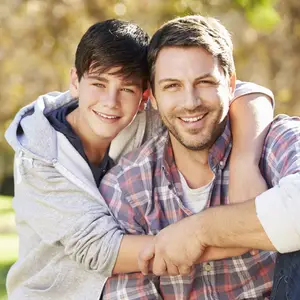 A father and son pose in a park with trees in the background.