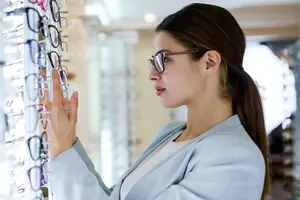 A woman is standing in front of a display of glasses and wearing glasses.