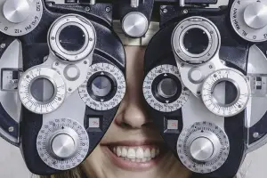 A woman is smiling while wearing an eye exam device with multiple dials and lenses