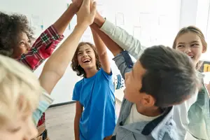 Six children gather to cheer each other on by putting their hands together in a huddle