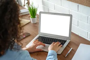 A woman typing on a laptop with a blank screen on a desk