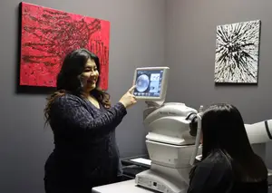 A woman demonstrates an eye exam machine while another woman looks through it.