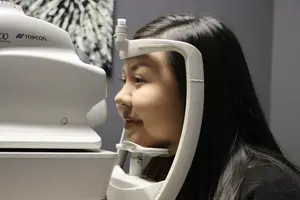 A woman wearing a black shirt is having her eyes examined with a Topcon camera.